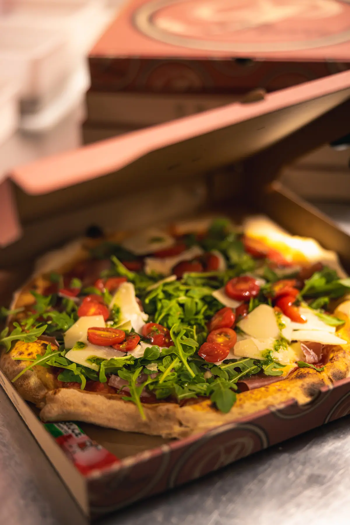 Pizza garnie de roquette, tomates et parmesan dans sa boîte à emporter
